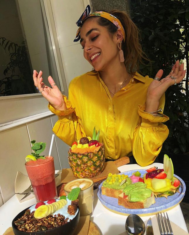 Vegan hotspot in Barcelona met fruit avocado banaan granola en een ananas met brood en koffie en een meisje met een gele top
